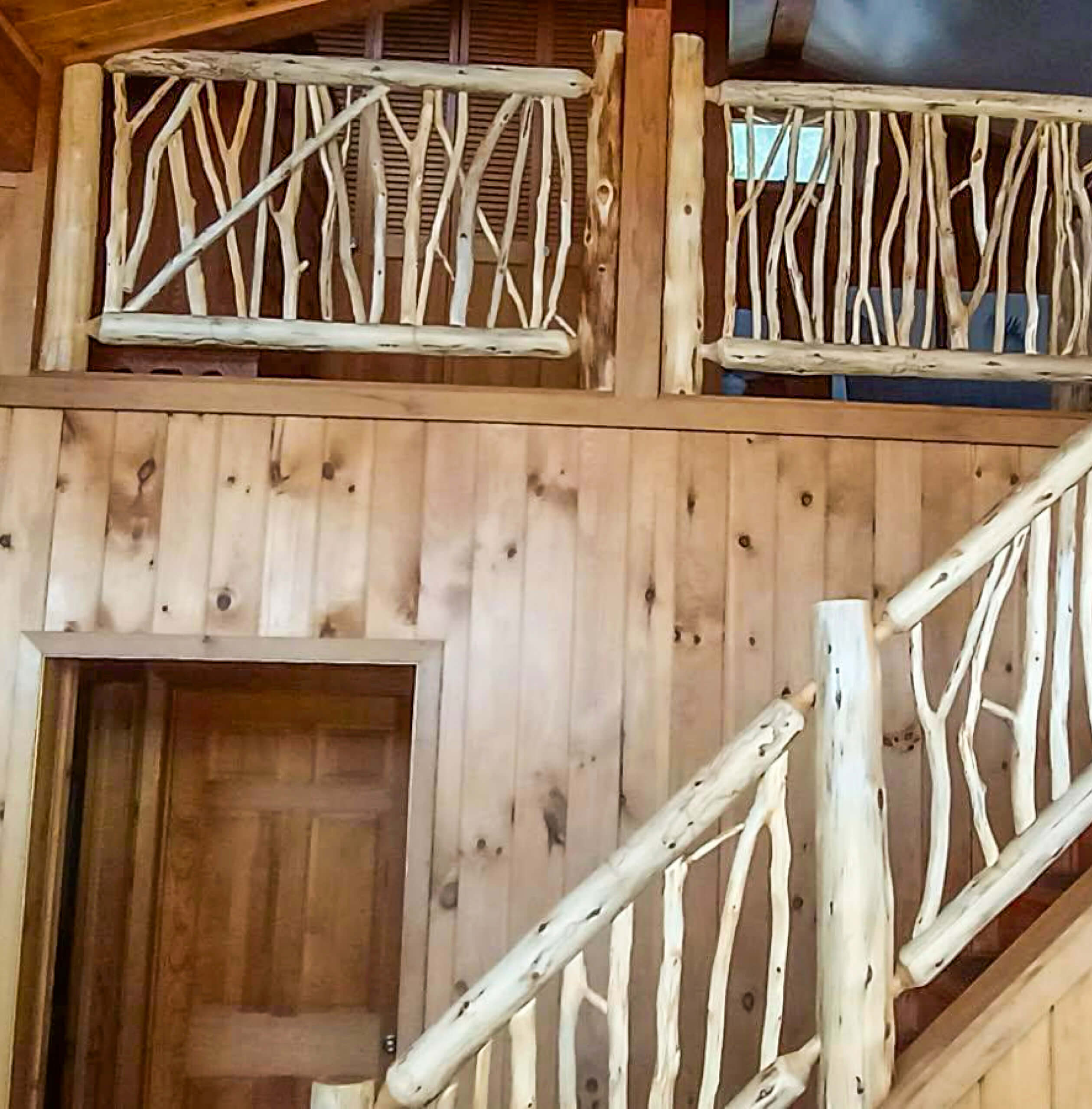 Brookview Builders Penn Yan, NY Interior view of a wooden cabin with natural log railings on the stairs and balcony, and wood-paneled walls and door.