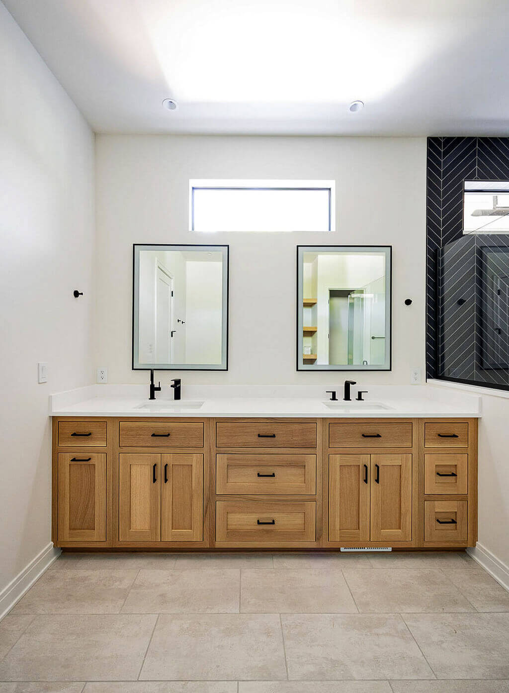Creative Cabinetry Bloomfield Iowa Modern bathroom with a double vanity featuring light wood cabinets, two rectangular mirrors, black fixtures, and neutral tile flooring.