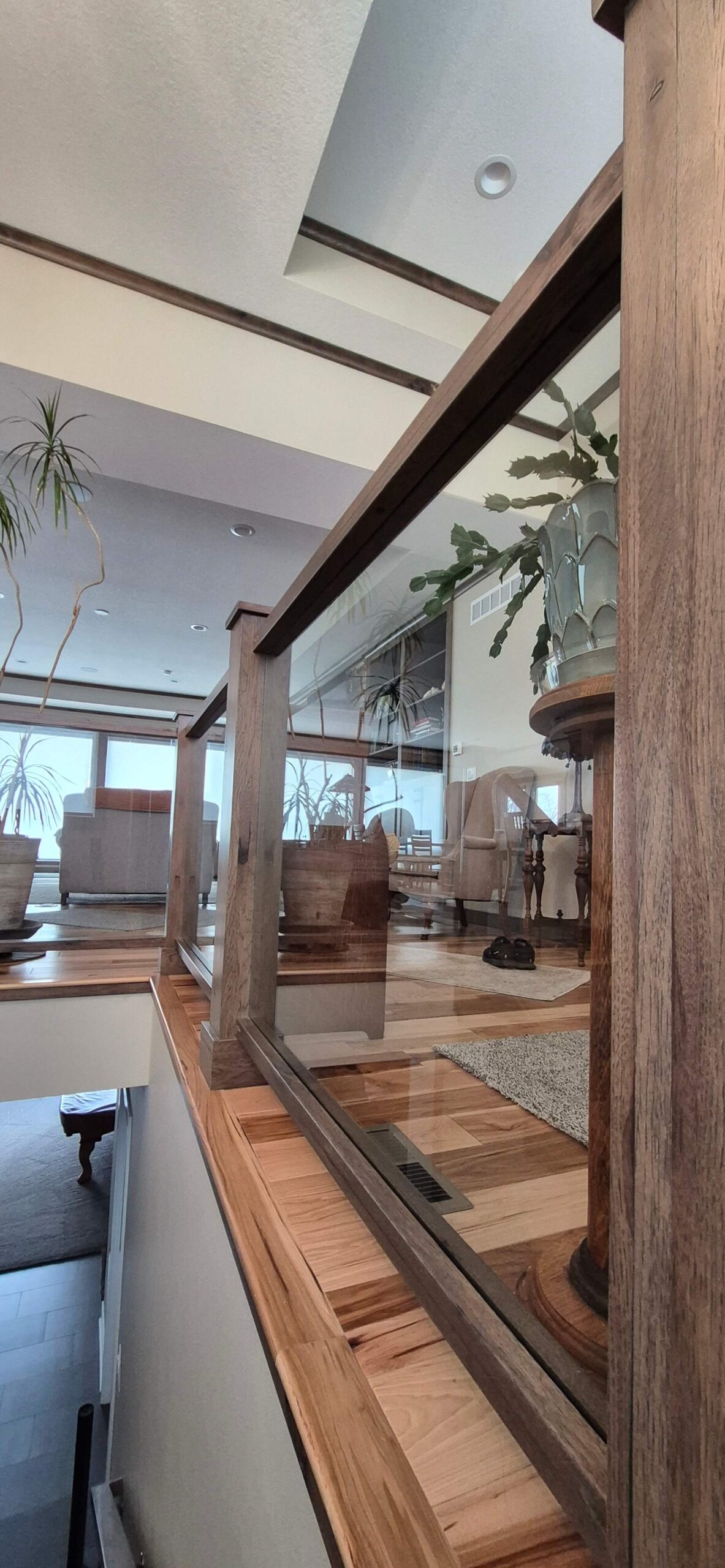 Creative Cabinetry Bloomfield Iowa A modern interior space with wooden floors, glass stair railing, potted plants, and large windows letting in natural light.