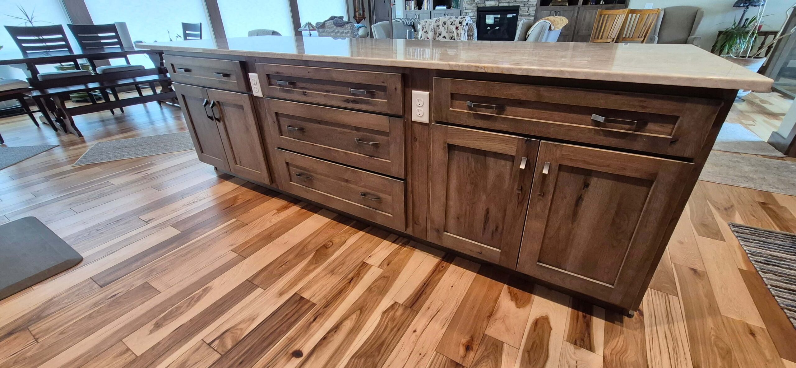 Creative Cabinetry Bloomfield Iowa A kitchen island with a marble countertop and multiple brown wooden drawers and cabinets, set on a polished hardwood floor.