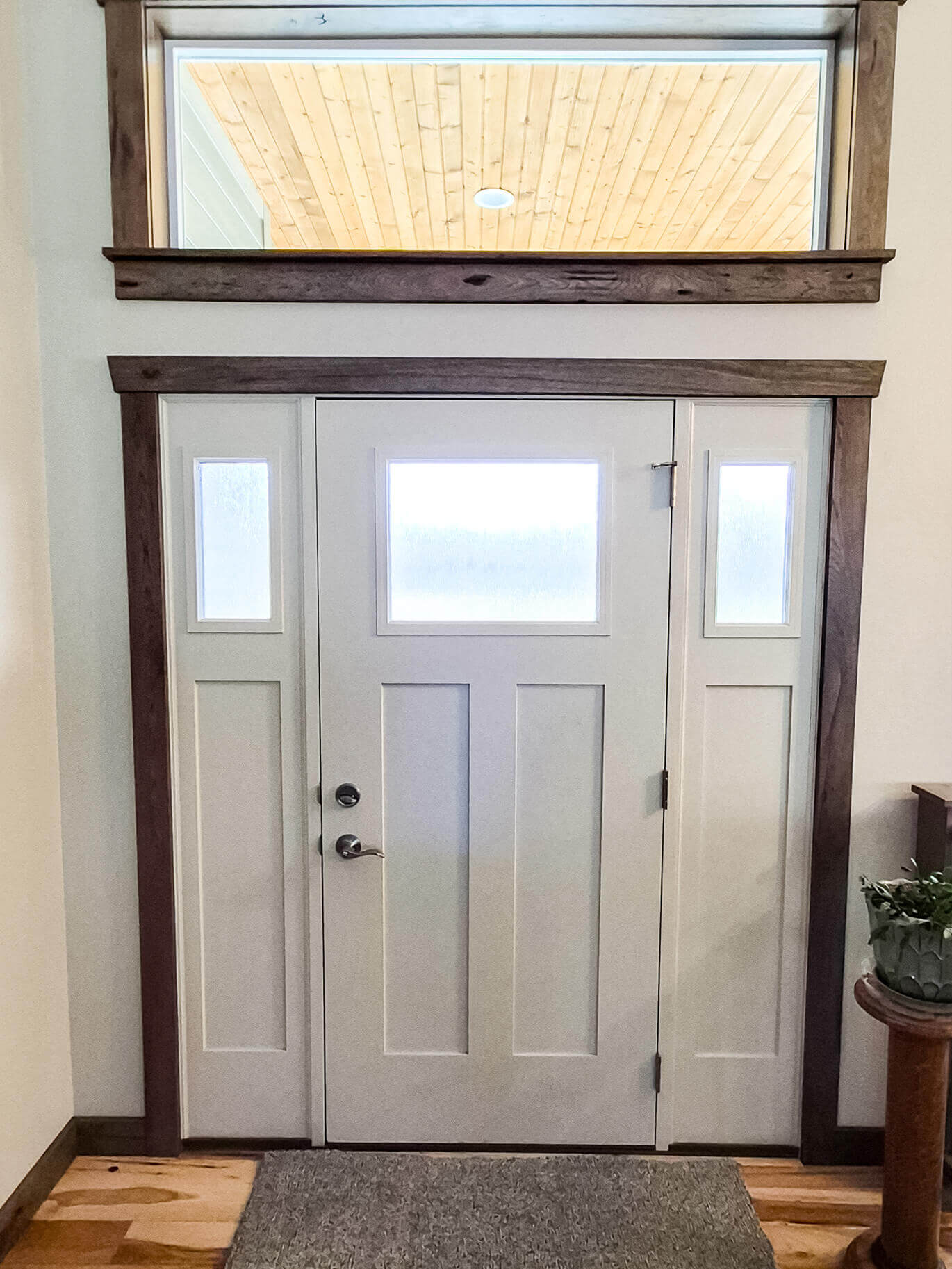 Creative Cabinetry Bloomfield Iowa White front door with three vertical panels and three frosted glass windows, set in a wooden frame with a large transom window above, inside a modern entryway.