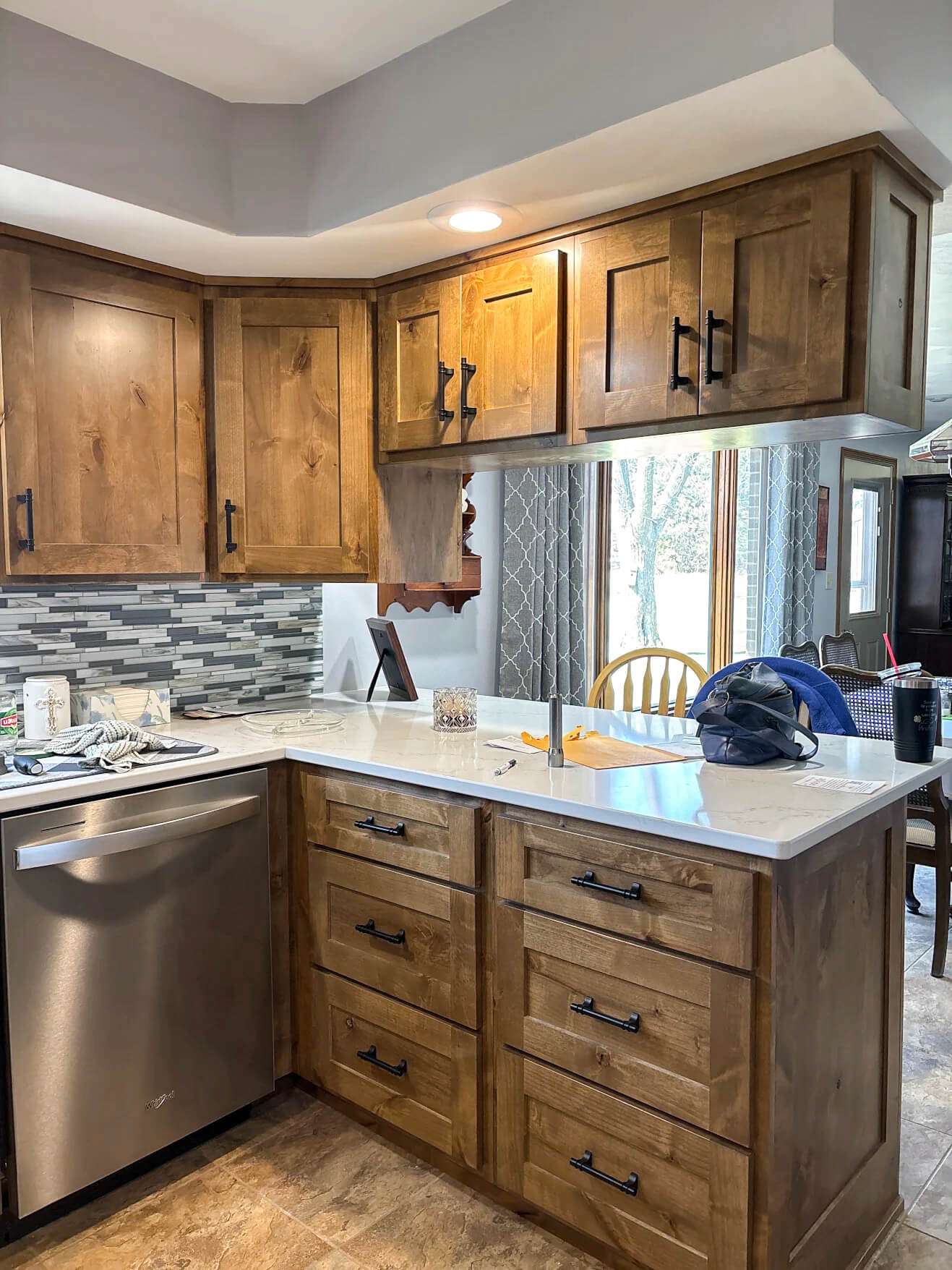 Creative Cabinetry Bloomfield Iowa A modern kitchen features wooden cabinets, a white countertop, a stainless steel dishwasher, and miscellaneous items on the counter.