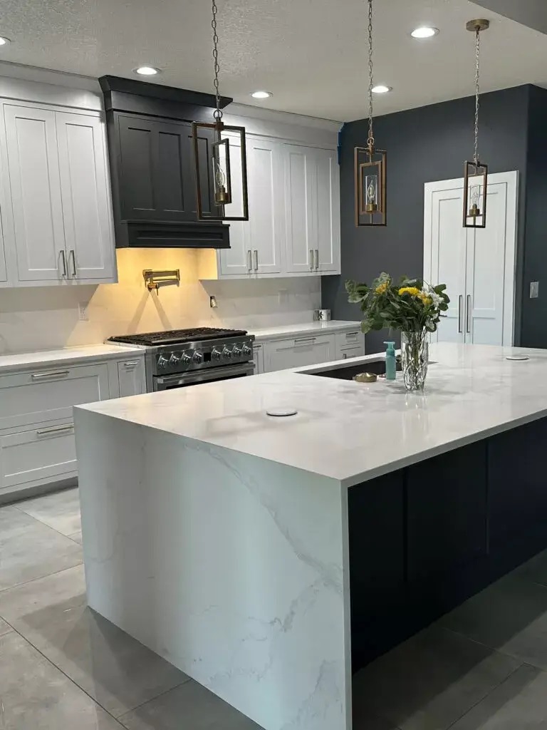 Creative Cabinetry Bloomfield Iowa Modern kitchen with white and black cabinetry, a marble island, pendant lights, stainless steel appliances, and a vase of flowers on the countertop.