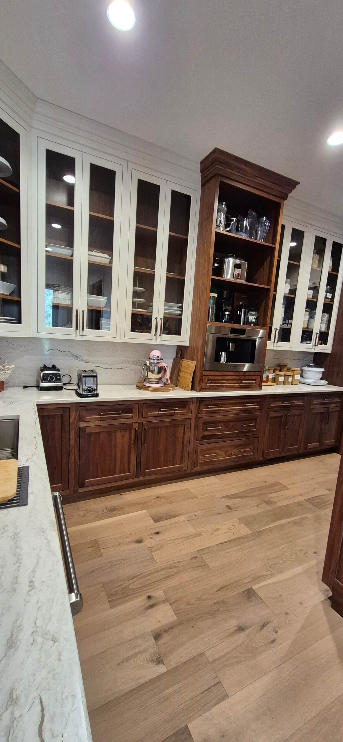 Creative Cabinetry Bloomfield Iowa A kitchen features glass-front upper cabinets, wood lower cabinets, a stand mixer, blender, toaster, built-in microwave, and light wood flooring.