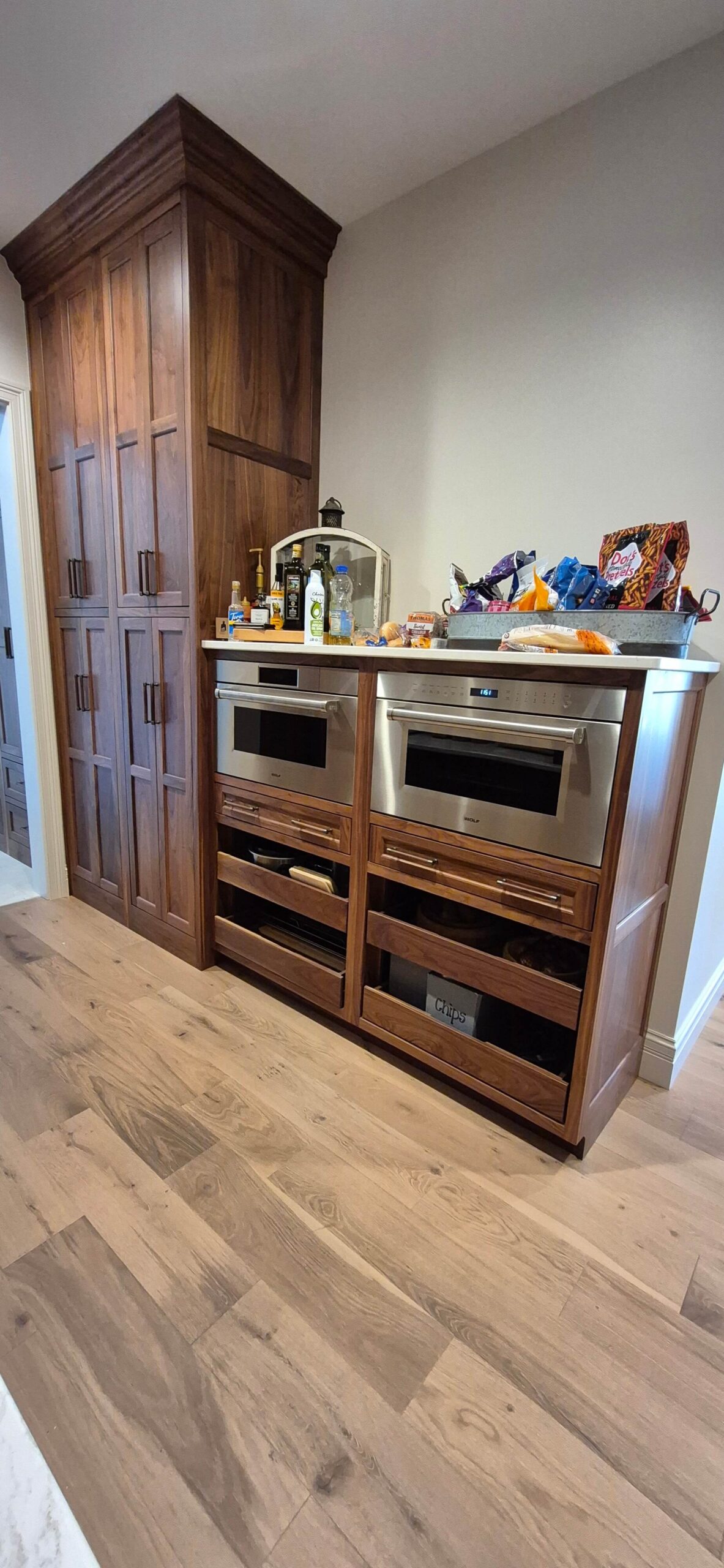 Creative Cabinetry Bloomfield Iowa A kitchen area with wooden cabinets, two built-in stainless steel appliances, and a countertop holding snacks, drinks, and small kitchen items.