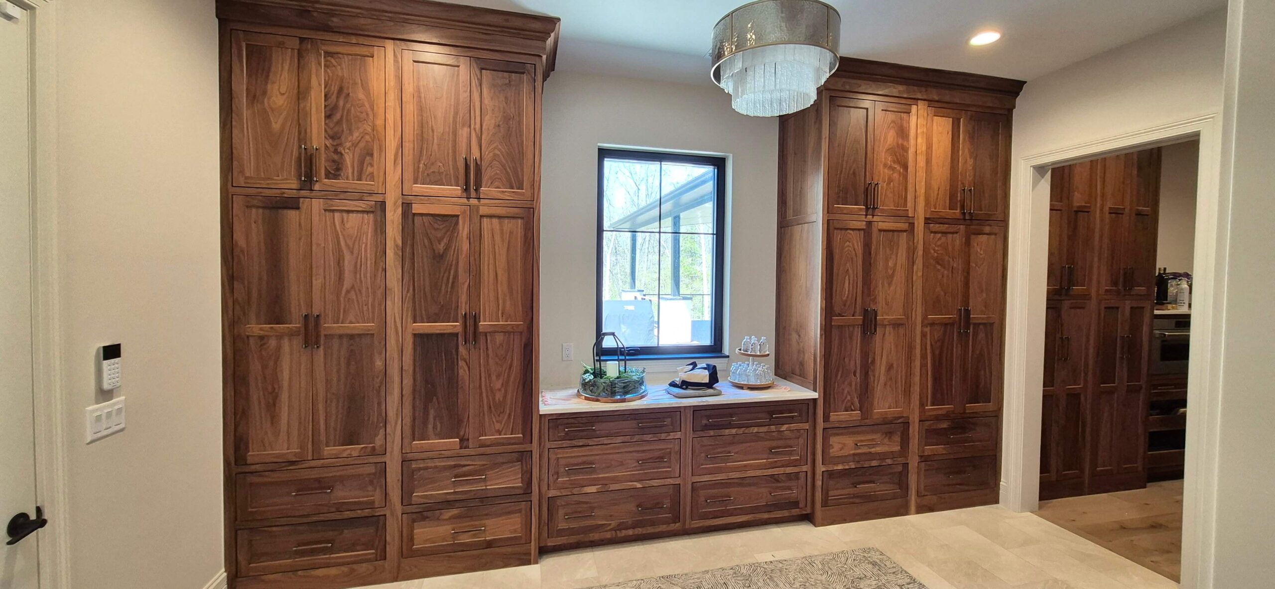 Creative Cabinetry Bloomfield Iowa Wooden cabinets with multiple drawers and cupboards line the wall; a countertop with decor sits beneath a window, and a chandelier hangs from the ceiling.