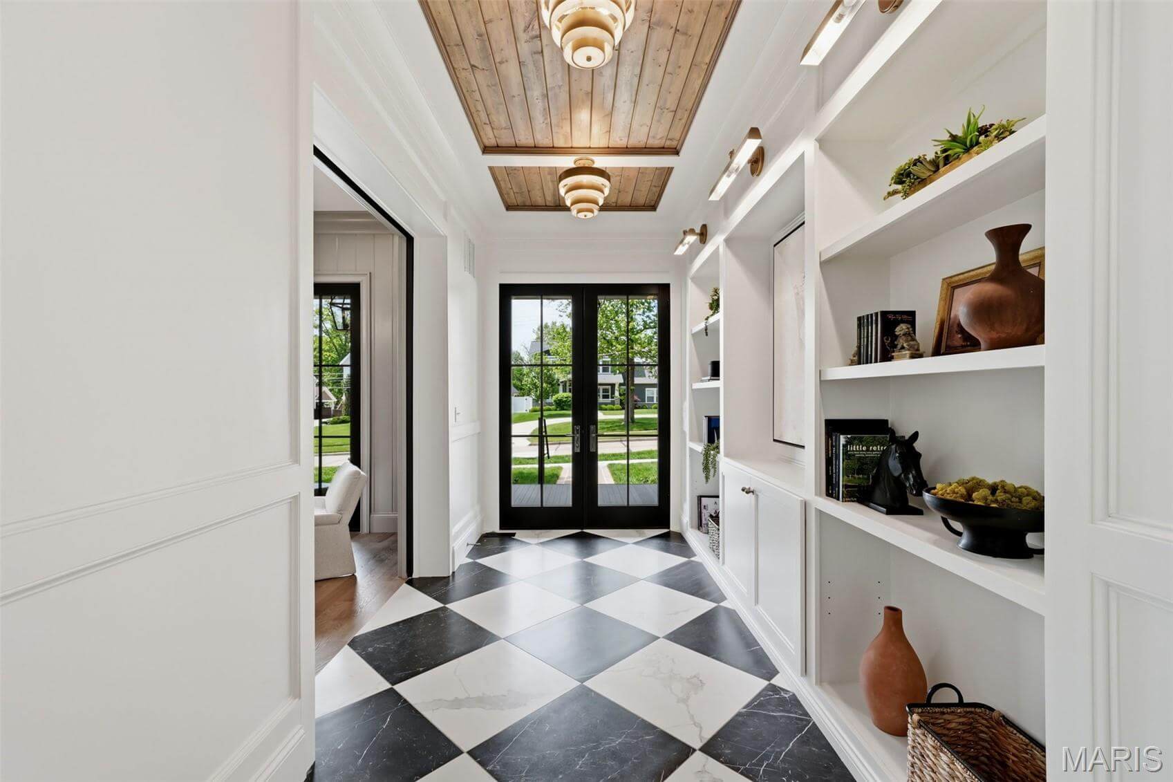 Kenrose Kitchens Custom Cabinetry Arthur IL Entryway with black and white checkered floor, built-in shelves with decor, wood-accented ceiling, and double glass doors leading outside.