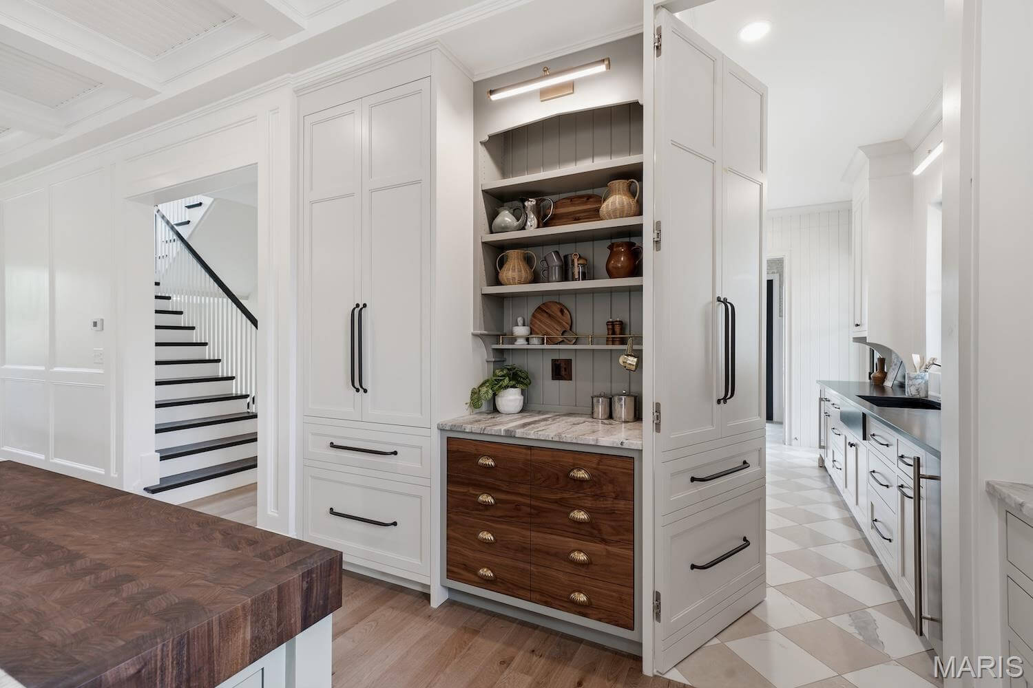 Kenrose Kitchens Custom Cabinetry Arthur IL A built-in kitchen cabinet with open shelves displays dishes and cookware; lower drawers have wood fronts and brass handles. White cabinetry and wood flooring are visible.