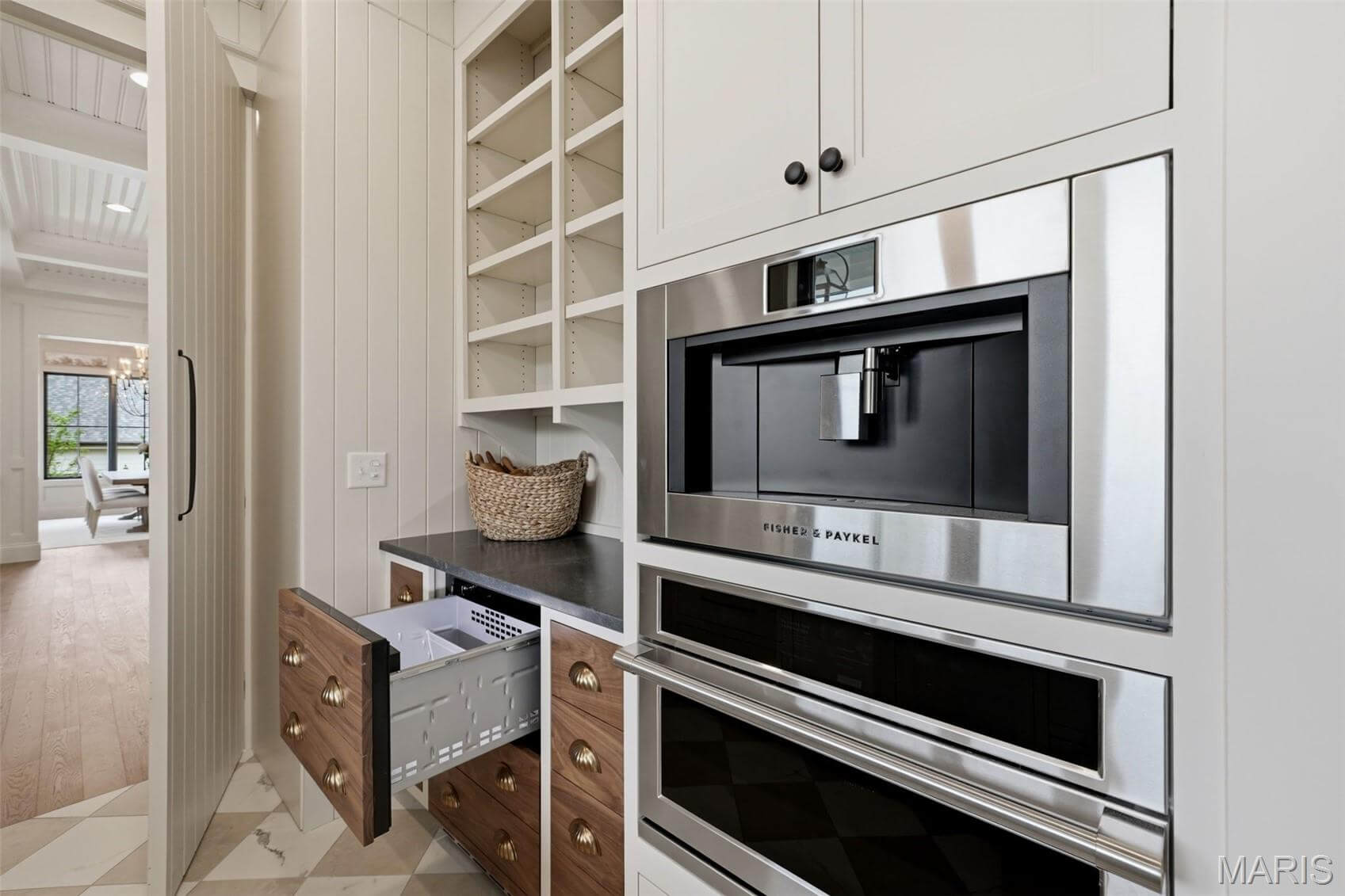 Kenrose Kitchens Custom Cabinetry Arthur IL Modern kitchen with built-in coffee maker, oven, open drawers, shelves, and a countertop with a basket; adjacent dining area visible through an open doorway.