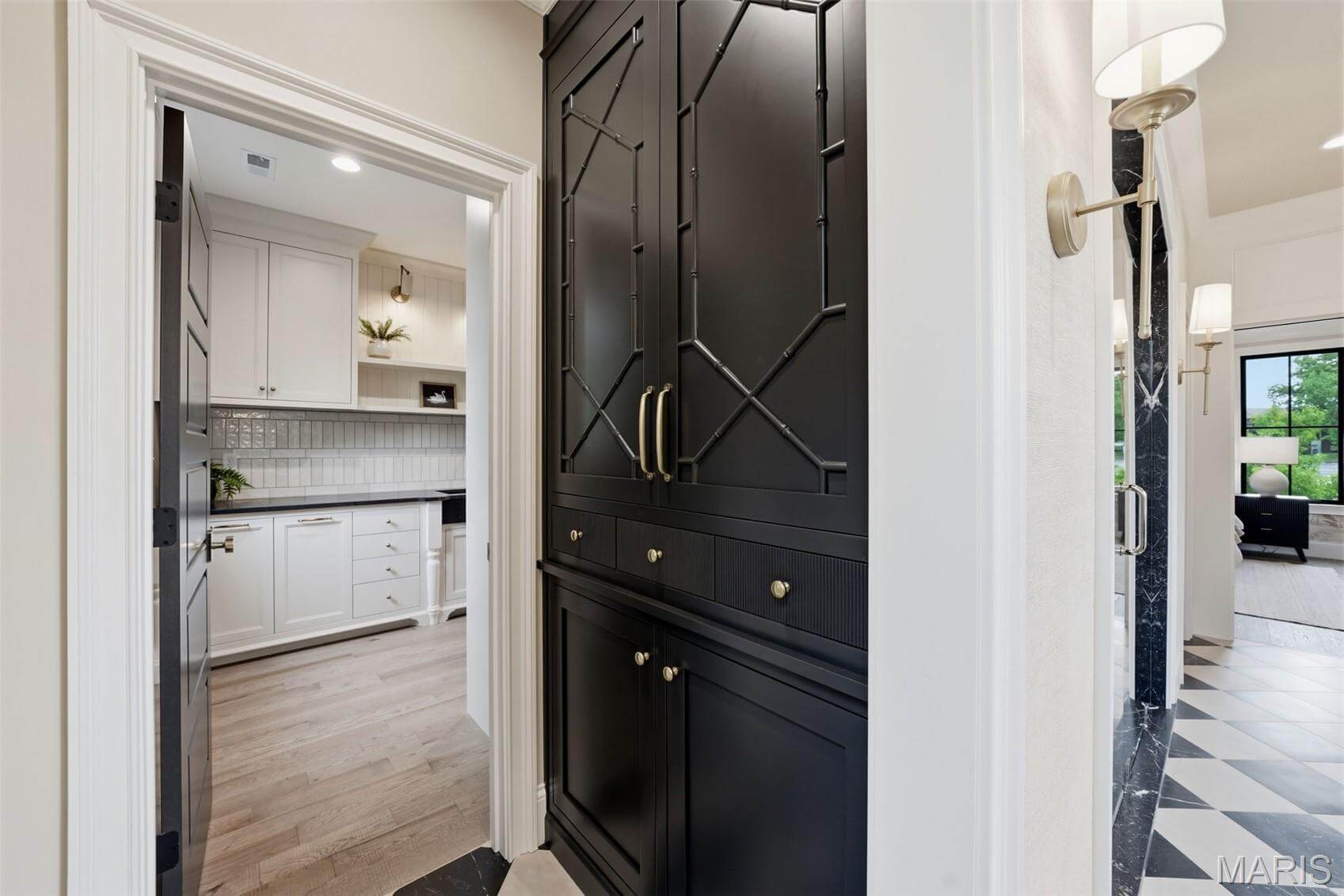 Kenrose Kitchens Custom Cabinetry Arthur IL A hallway with black built-in cabinets leads to a white kitchen with tile backsplash and connects to a living room with large windows.