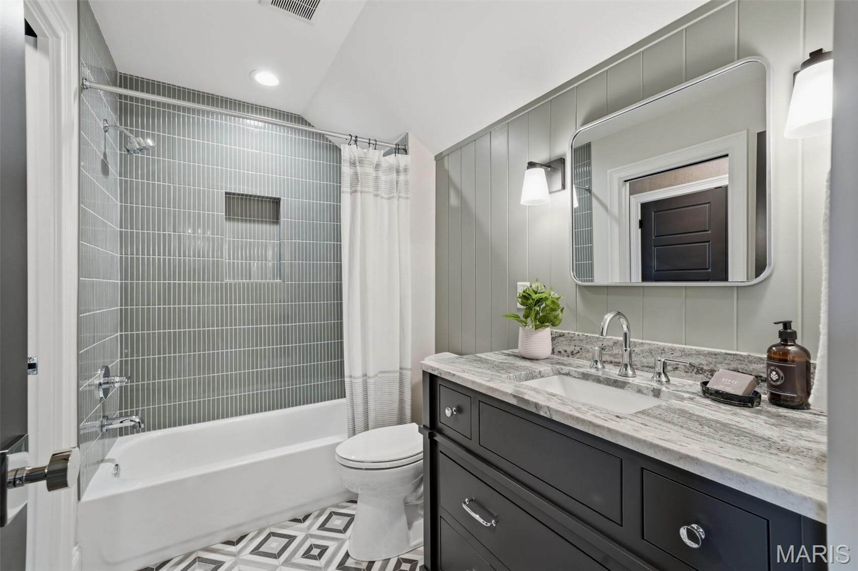 Kenrose Kitchens Custom Cabinetry Arthur IL Modern bathroom with a bathtub and shower, gray tile walls, patterned floor, dark vanity with granite countertop, and a wall-mounted mirror above the sink.