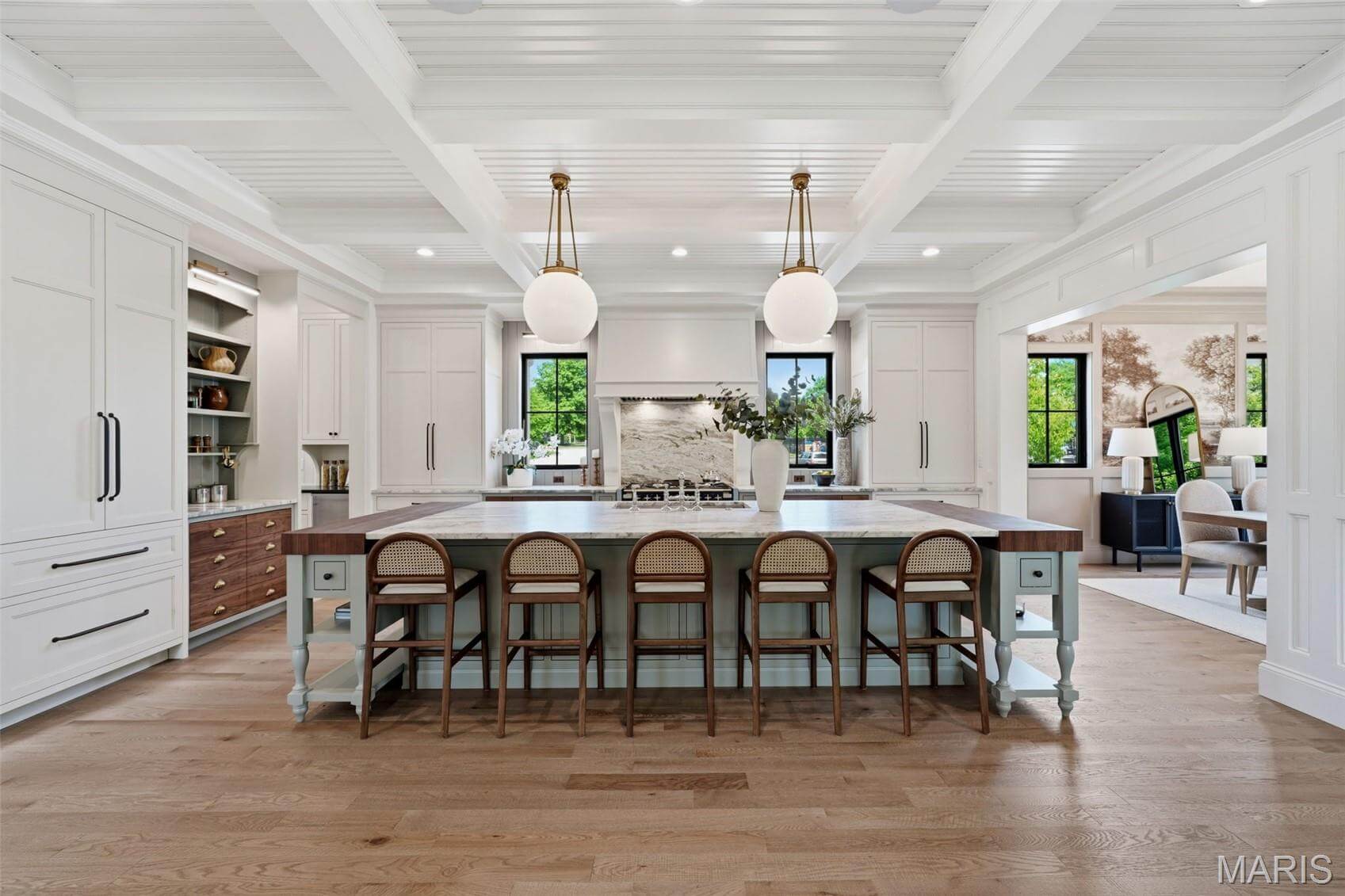 Kenrose Kitchens Custom Cabinetry Arthur IL Spacious modern kitchen with a large island, five stools, pendant lights, white cabinetry, wood floors, and open views to adjoining rooms.