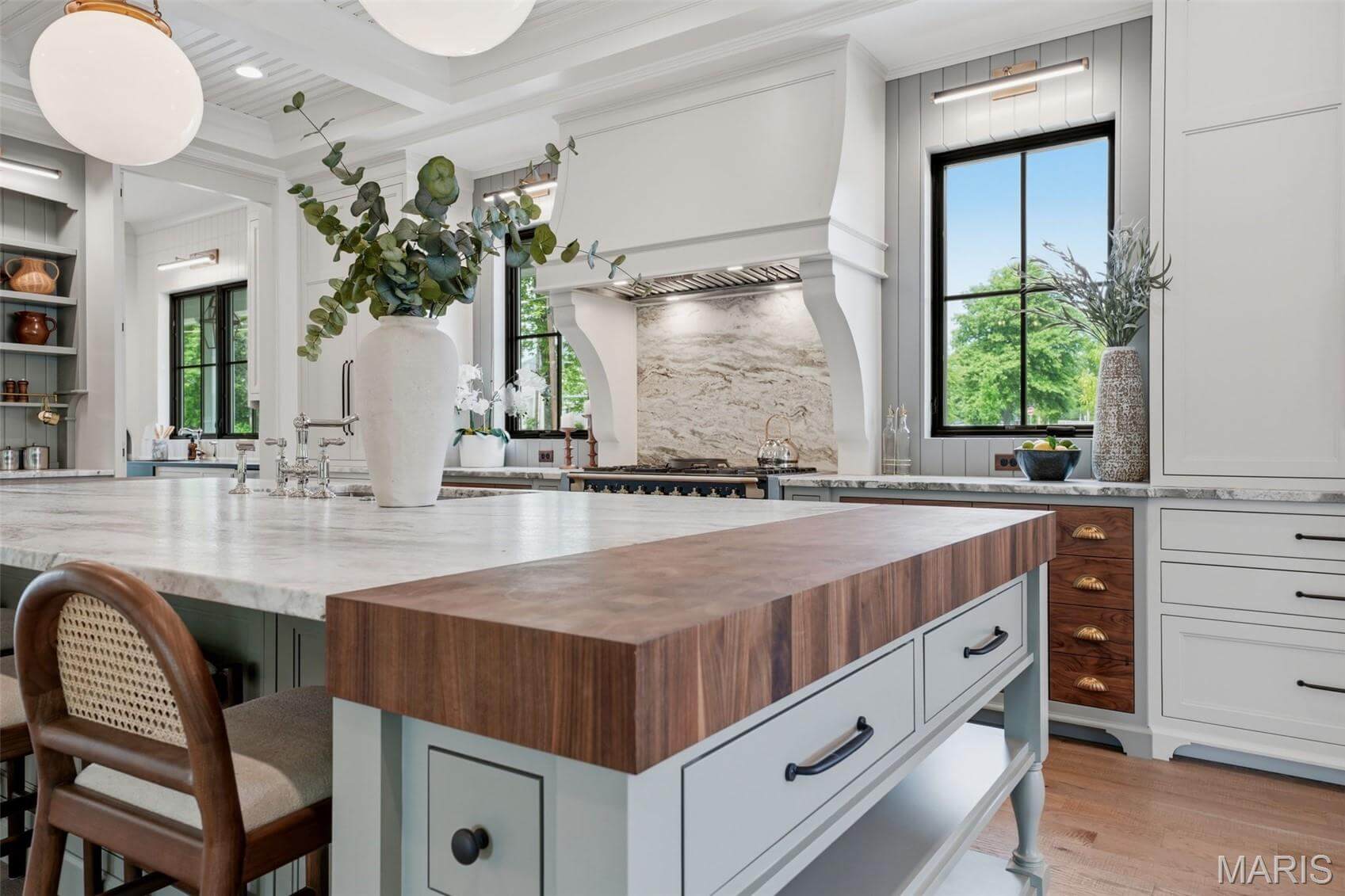 Kenrose Kitchens Custom Cabinetry Arthur IL Bright, modern kitchen with a large island featuring a wood butcher block, marble countertops, built-in stove, range hood, and large windows letting in natural light.