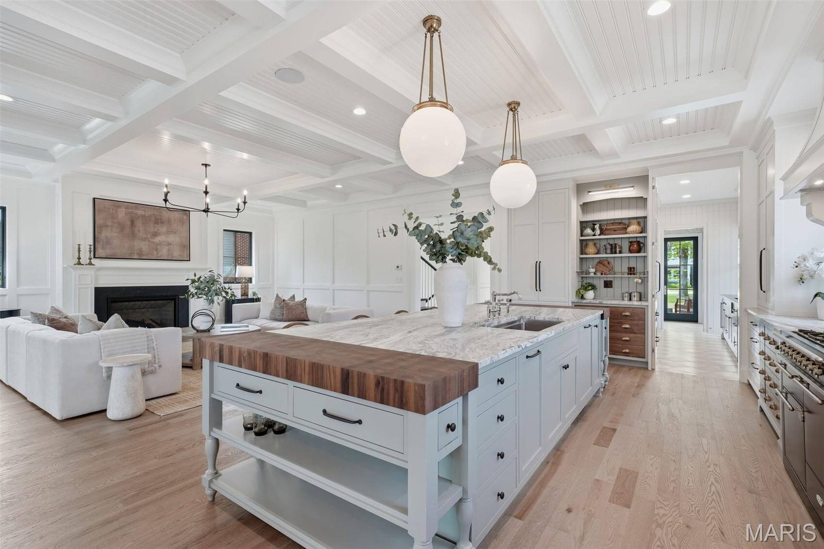Kenrose Kitchens Custom Cabinetry Arthur IL Spacious modern kitchen with a large island, light blue cabinetry, wood and marble countertops, pendant lights, and an open living area with a fireplace in the background.