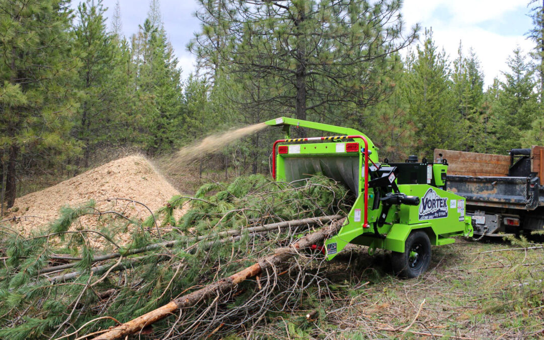 Treeco Tree Service Clayton, WA A wood chipper machine processes tree branches, ejecting wood chips into a pile in a forested area.
