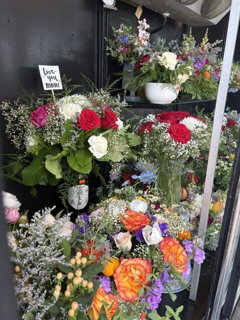 Swampy Hollow Greenhouse Gallery Cochranville, PA Several bouquets of colorful flowers, including roses and mixed blooms, are displayed on shelves. One bouquet has a small sign that reads "love you mom.