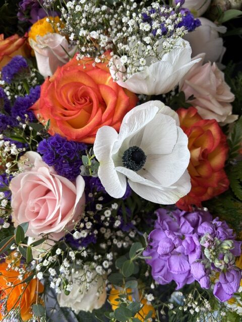 Swampy Hollow Greenhouse Gallery Cochranville, PA A close-up of a mixed bouquet featuring orange and pink roses, white anemone, purple flowers, and baby's breath.