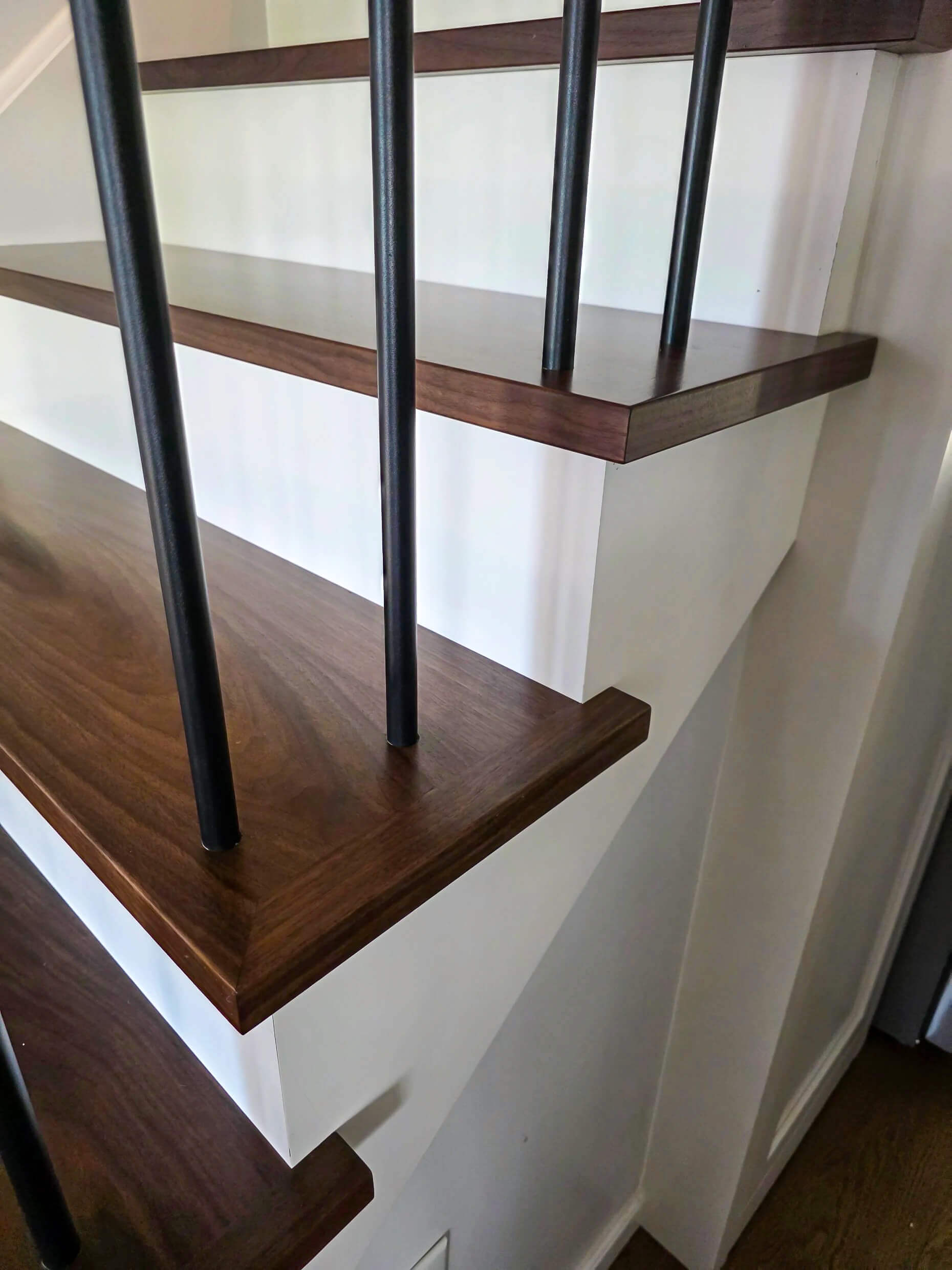Brookview Builders Penn Yan, NY Close-up view of modern stairs with dark wooden treads, white risers, and vertical black metal railings.