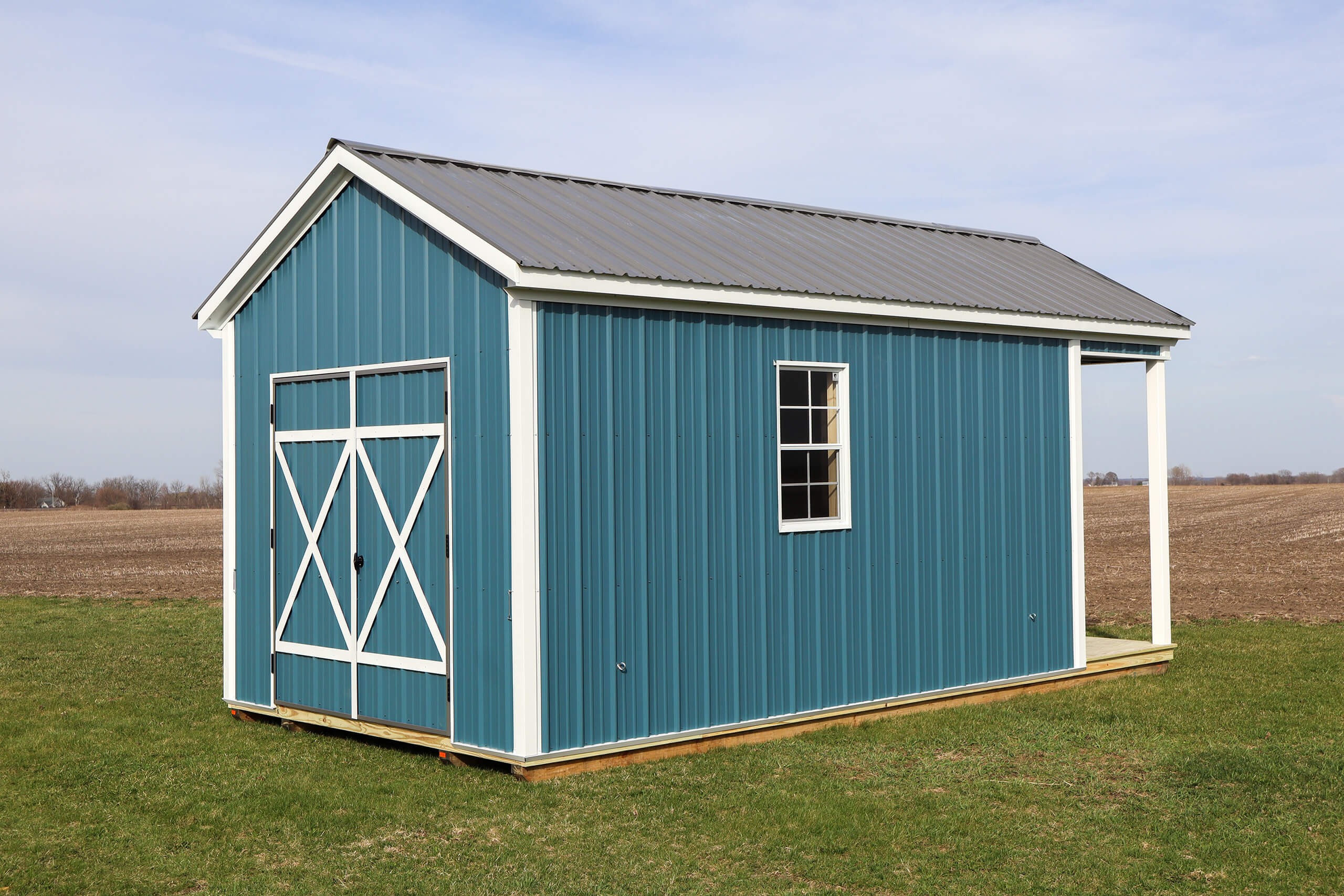 A small blue metal shed with a barn-style door and a window stands on a grassy field under a partly cloudy sky.