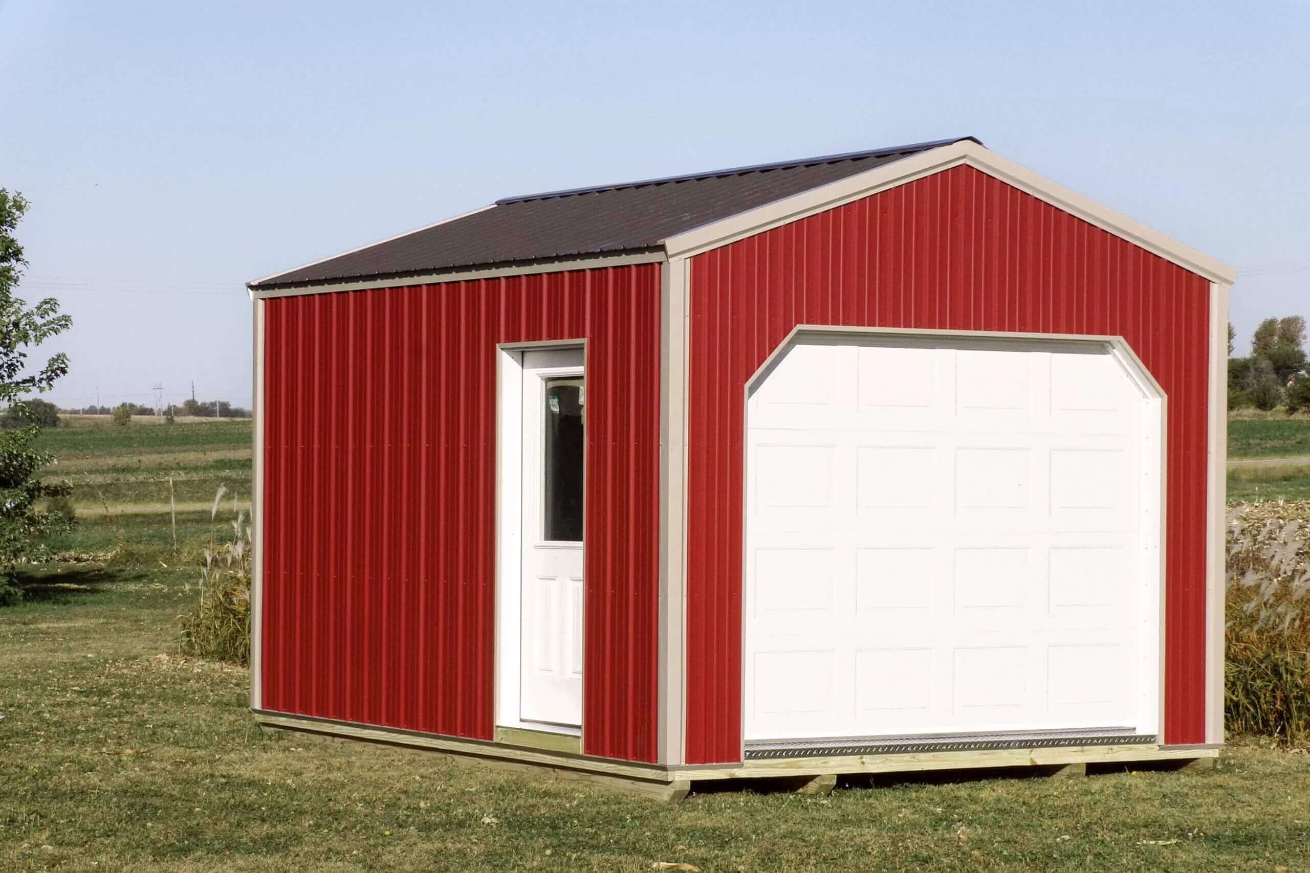 A small red shed with a white door and garage door sits on grass in a rural outdoor setting.