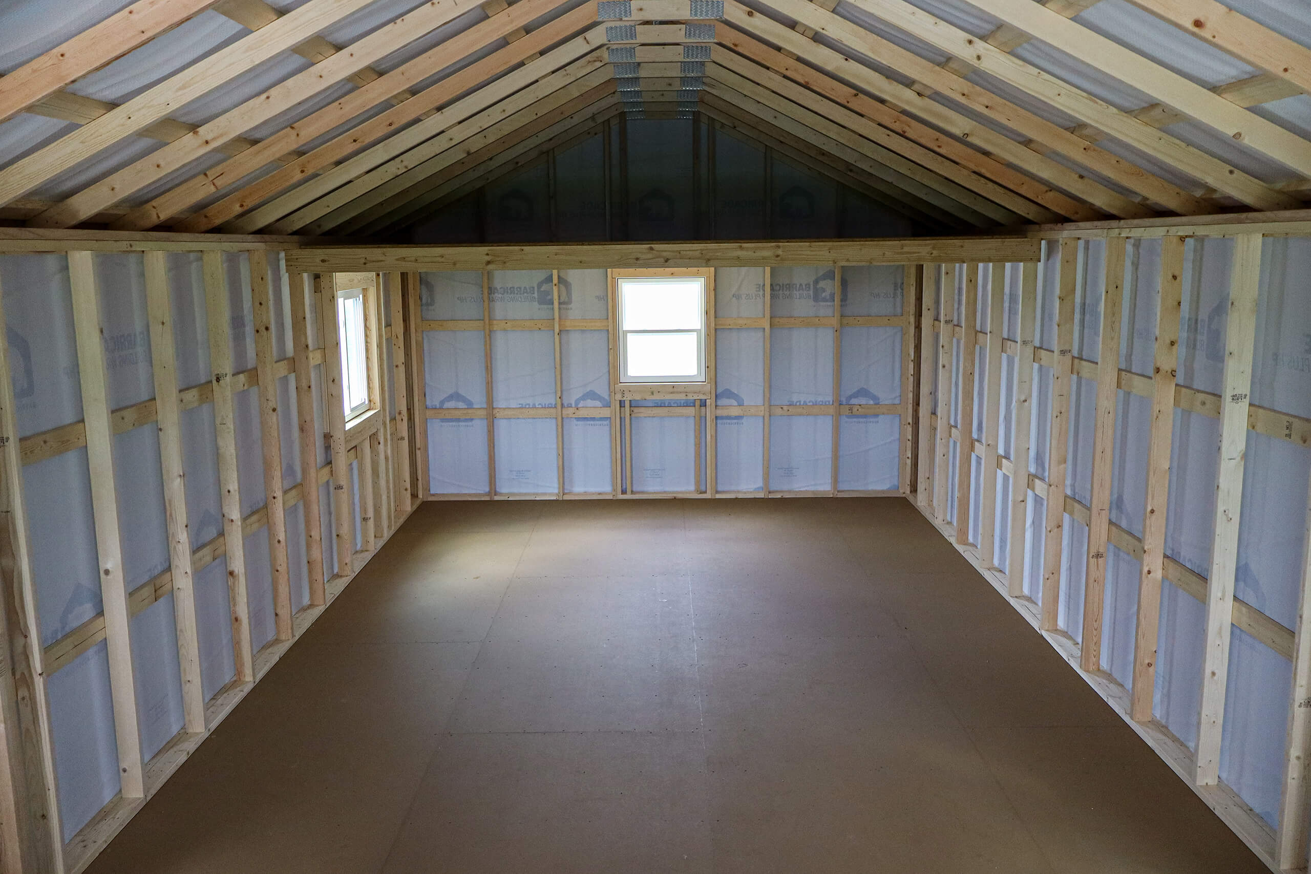 Unfinished attic with exposed wooden framing, insulated walls, and two small windows at the far end. No flooring or fixtures installed.