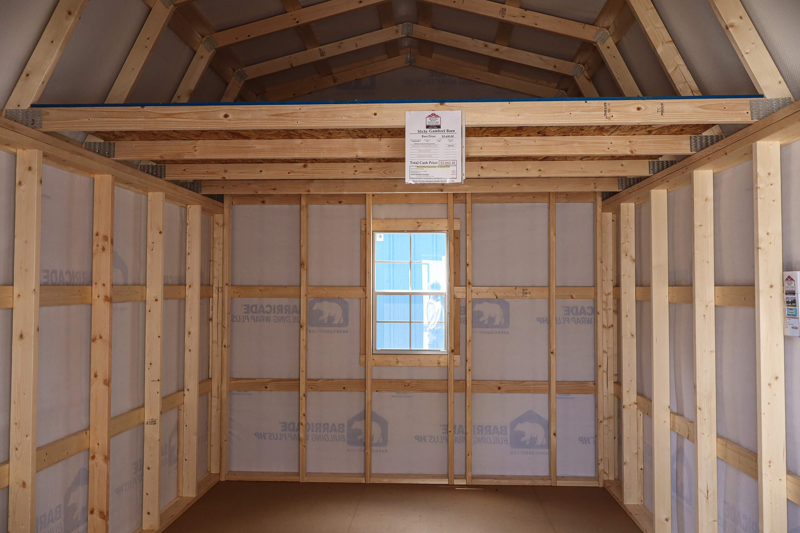 Unfinished wooden shed interior with exposed framing and insulation, one small window at the center, and a paper notice posted above the window.