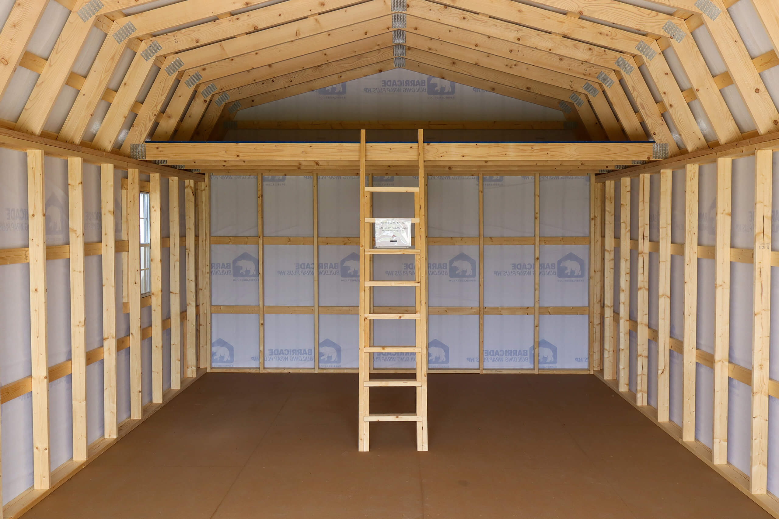 The interior of a wooden shed with exposed framing, a plywood floor, a small loft, and a ladder leading up to the loft.