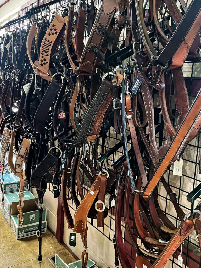 Penchem Tack Store Guthrie, KY Several leather horse bridles and straps hanging on a metal grid wall display in a tack shop, with storage boxes stacked below.