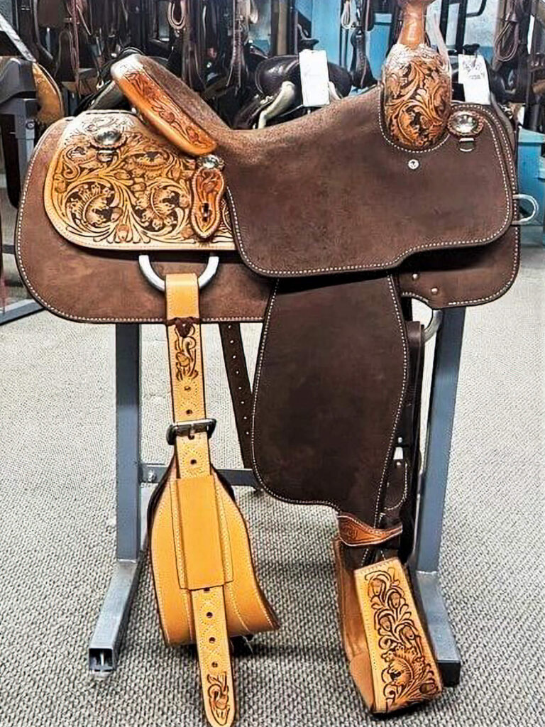 Penchem Tack Store Guthrie, KY Brown leather western saddle with intricate floral tooling, displayed on a saddle stand in a store setting.