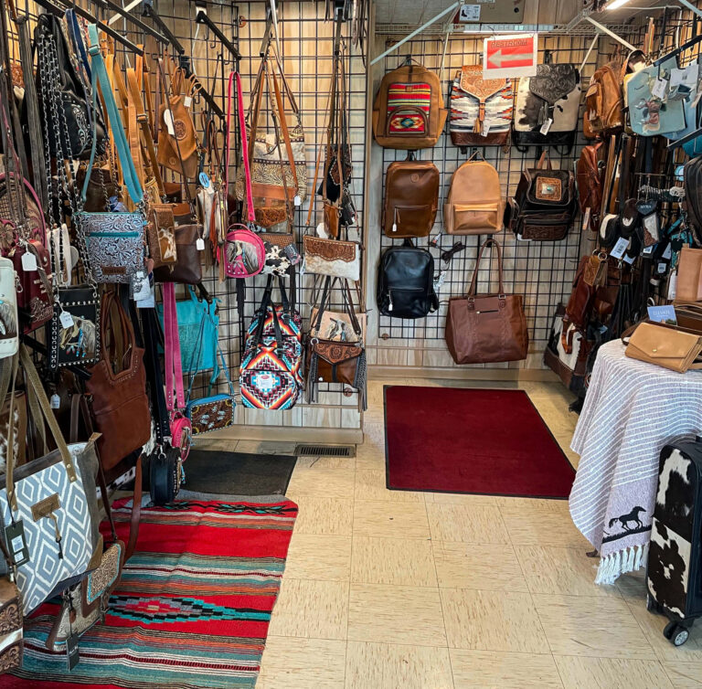 Penchem Tack Store Guthrie, KY Display of assorted handbags and purses in various colors and styles hanging on racks in a store, with rugs and tiled flooring visible.