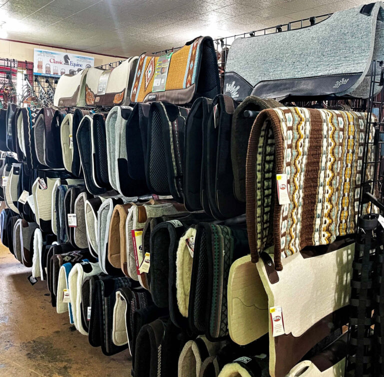 Penchem Tack Store Guthrie, KY A display of various saddle pads in different colors and patterns is arranged on racks inside a tack or feed store.