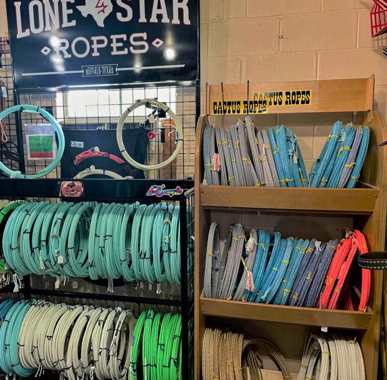 Penchem Tack Store Guthrie, KY Display of coiled ropes in various colors on shelves, with signs reading "Lone Star Ropes" and "Cactus Ropes" against a beige brick wall.