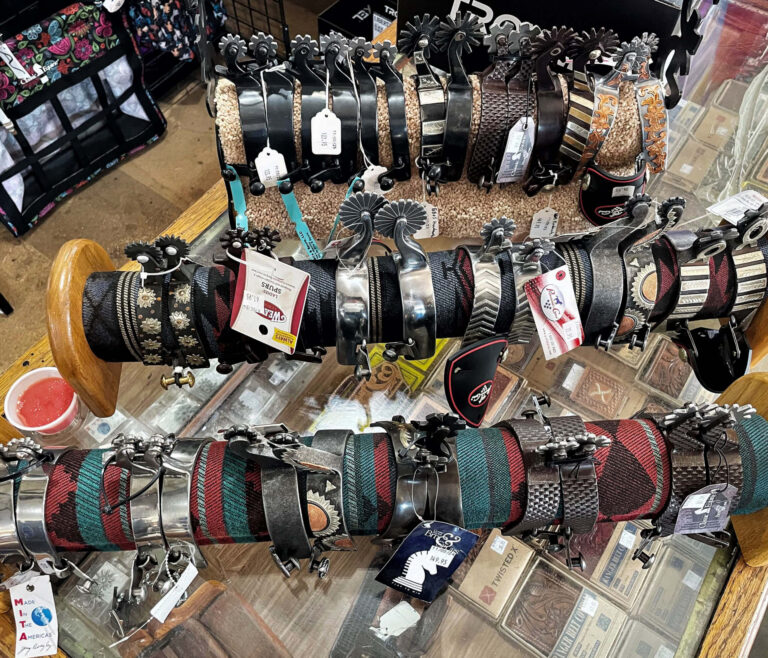 Penchem Tack Store Guthrie, KY Several rows of various patterned belts and buckles are displayed on racks atop a glass counter in a store.