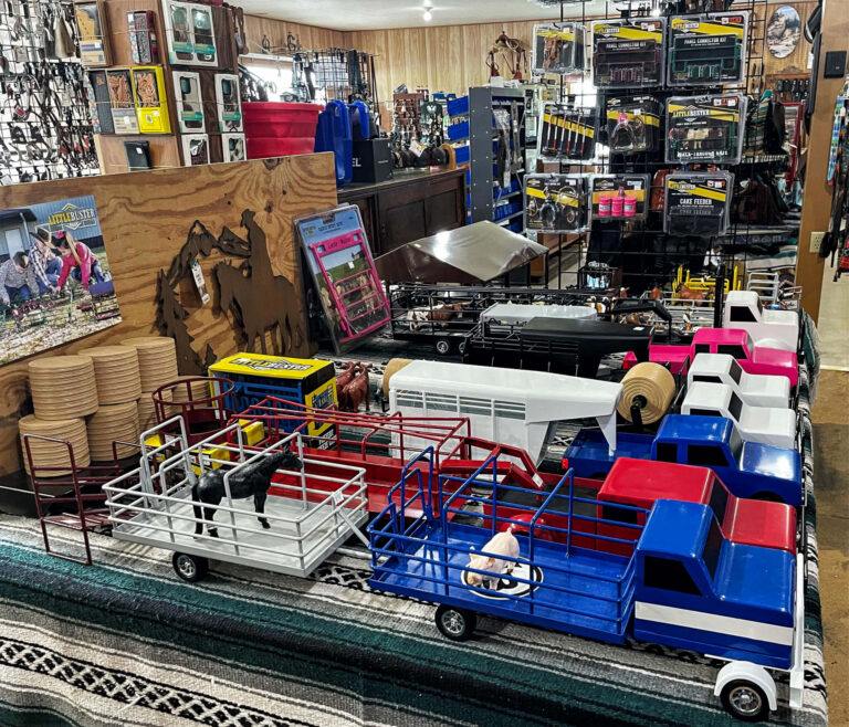 Penchem Tack Store Guthrie, KY Toy trucks and livestock trailers are displayed on a table in a store, with miniature animals inside. Shelves in the background hold various packaged items and accessories.