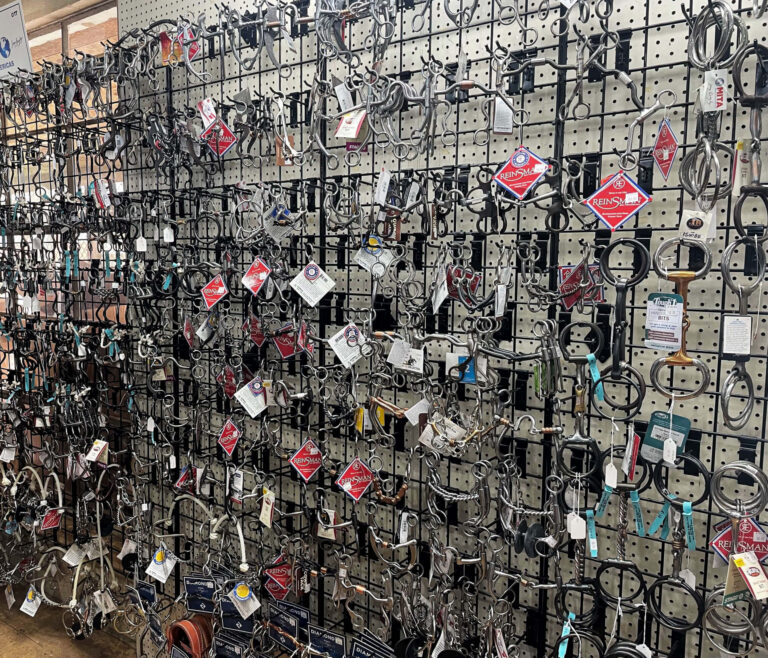 Penchem Tack Store Guthrie, KY A display wall of various horse bits and bridles organized on metal hooks in a tack shop.