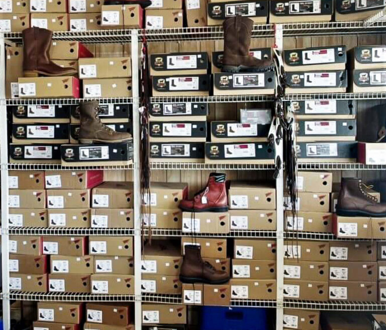 Penchem Tack Store Guthrie, KY Shelves filled with stacked boxes of boots, with several pairs of boots displayed on top of and in front of the boxes.