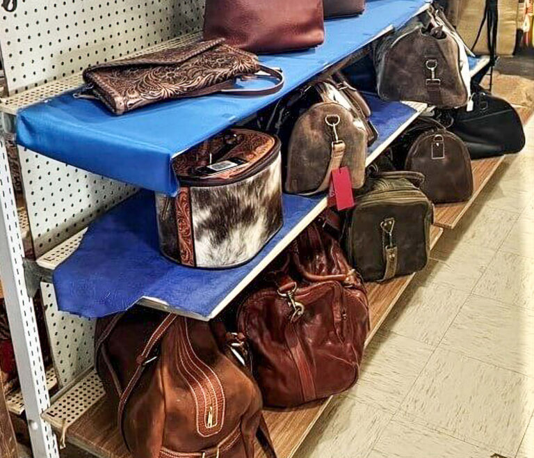 Penchem Tack Store Guthrie, KY Several leather and faux leather handbags, purses, and a hat box are displayed on blue shelves in a store.