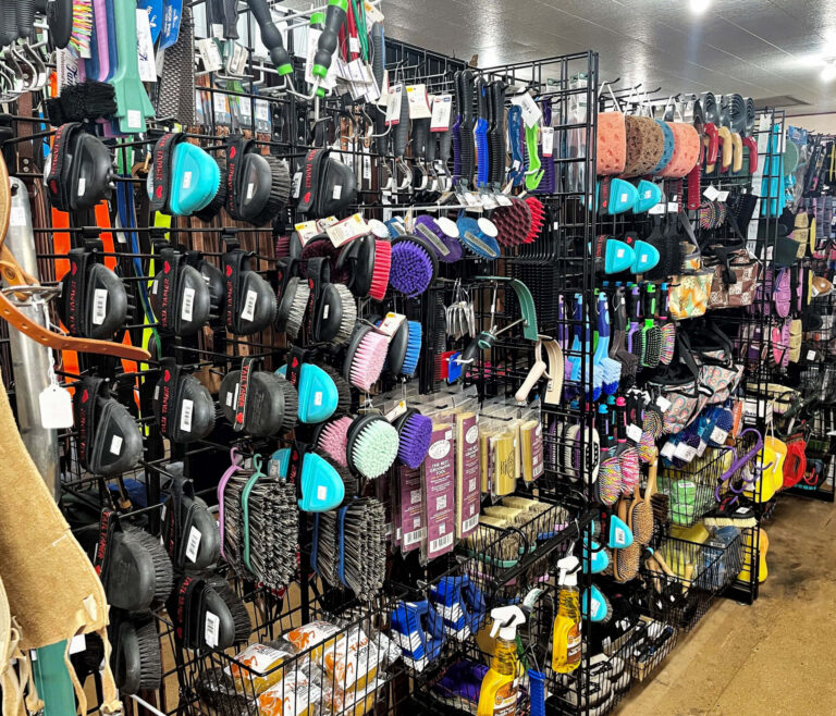 Penchem Tack Store Guthrie, KY Shelves display various pet grooming brushes, combs, sprays, and grooming tools arranged in organized rows in a store aisle.