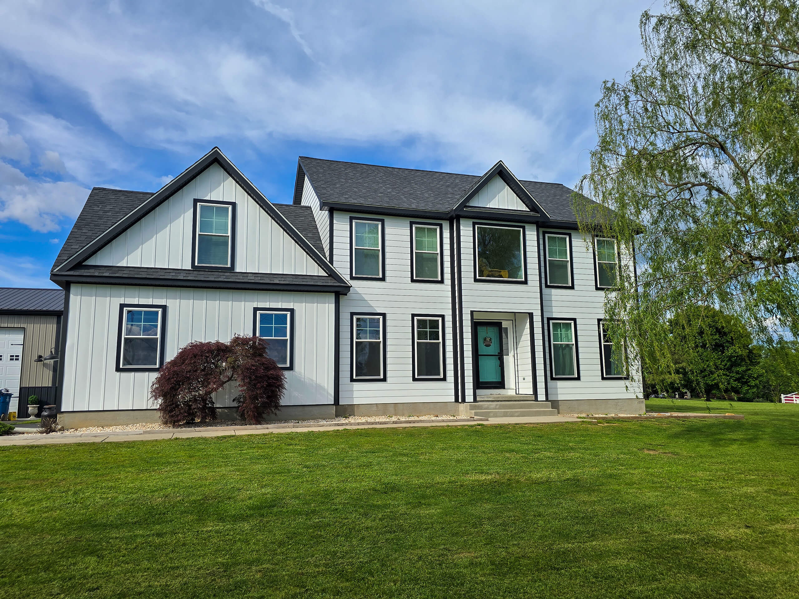 Blue Ridge Windows & Doors Quarryville Pennsylvania Two-story white house with black roof, teal front door, and large windows, surrounded by a green lawn, trees, and partly cloudy sky.