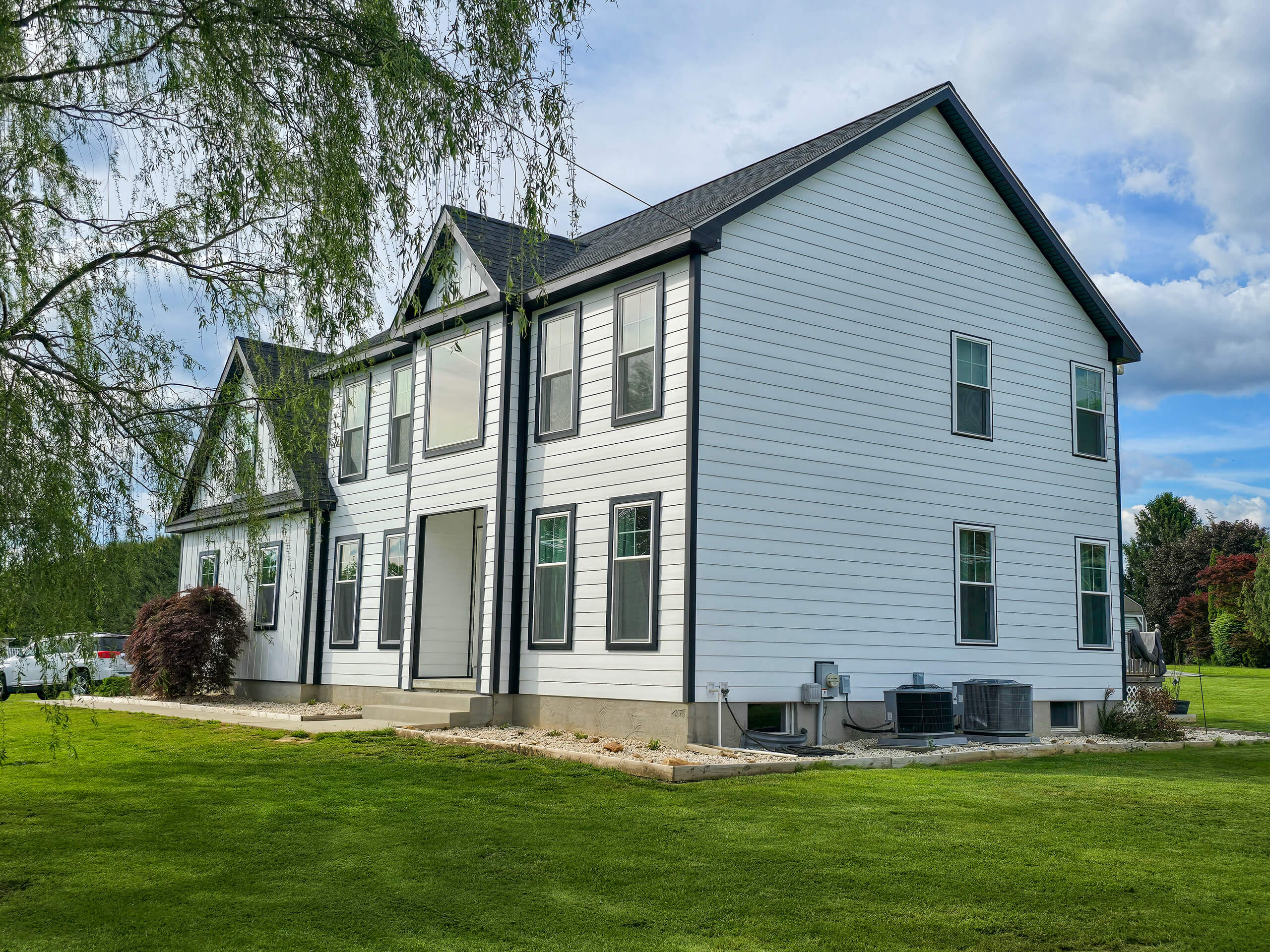 Blue Ridge Windows & Doors Quarryville Pennsylvania A modern two-story white house with black trim, multiple windows, and a well-maintained lawn under a partly cloudy sky.