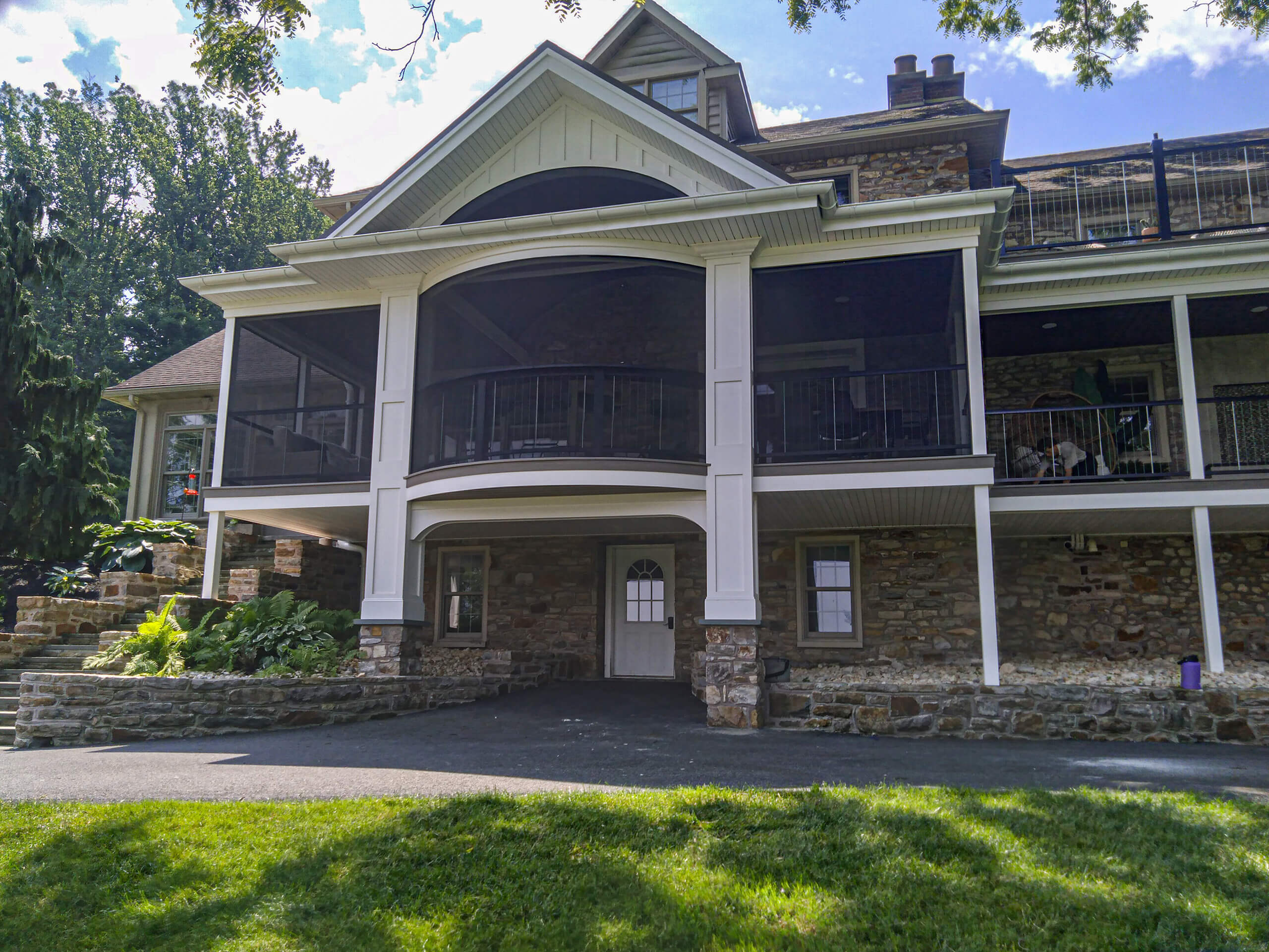 Blue Ridge Windows & Doors Quarryville Pennsylvania A large stone house with a screened-in porch, white columns, and a covered entryway, surrounded by trees and grass.