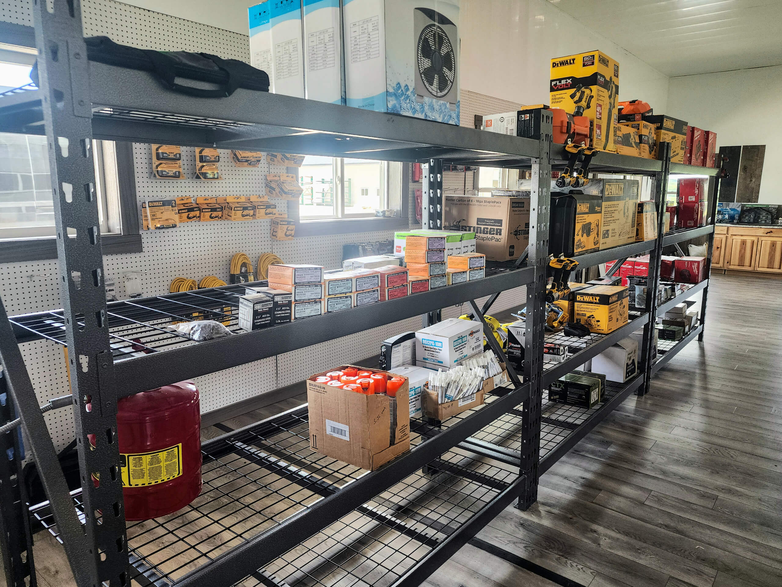 Sunset Metal Roofing and Siding Show Room Ebensburg, PA Shelves displaying various power tools, hardware, and boxes inside a well-lit store with wood flooring and a window in the background.