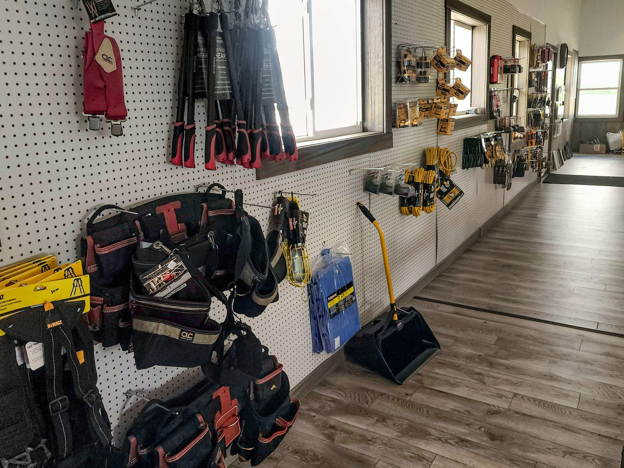Sunset Metal Roofing and Siding Show Room Ebensburg, PA Pegboard wall with various hand tools, tool belts, and accessories displayed in a well-lit room with wood flooring.