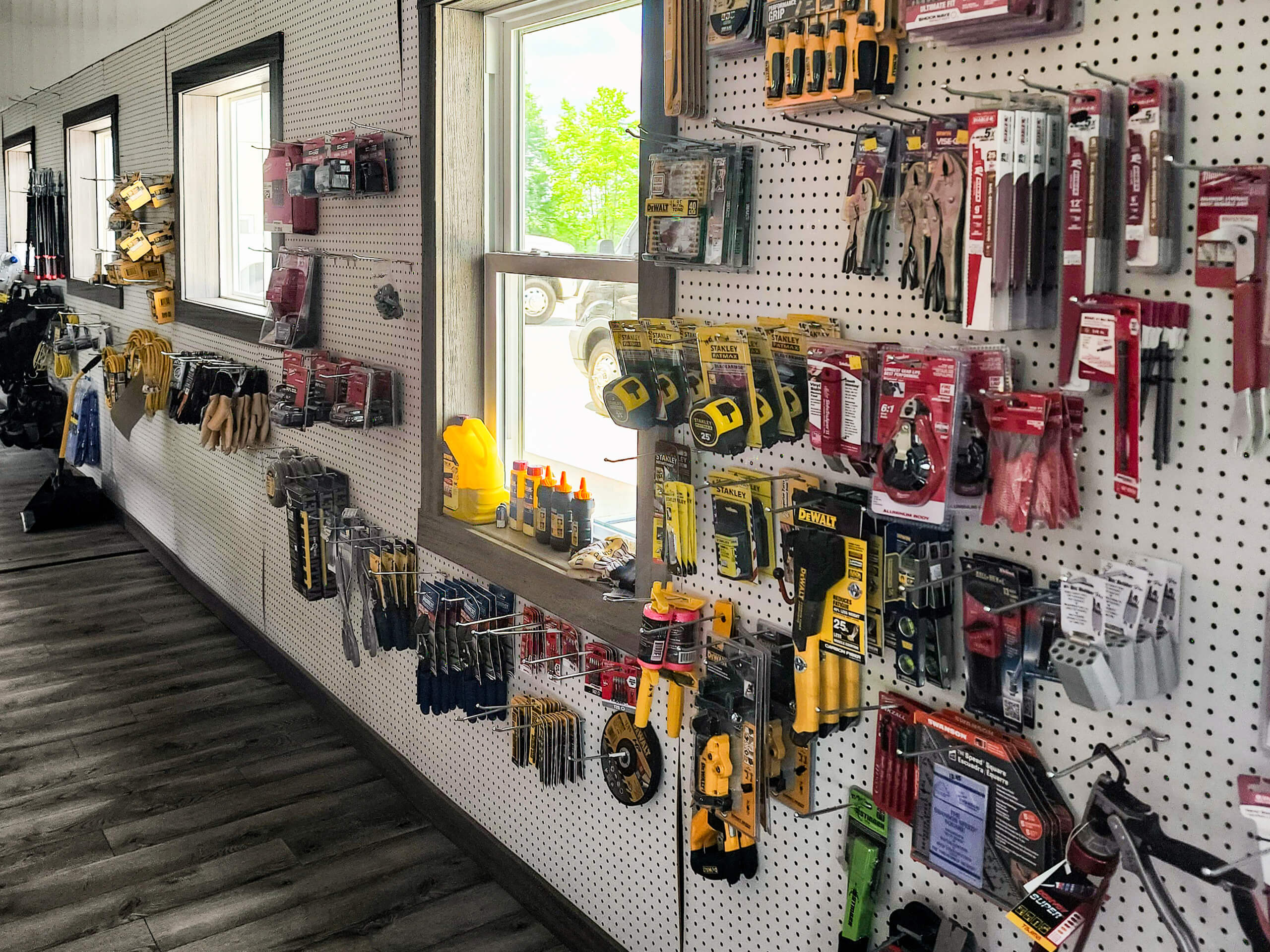 Sunset Metal Roofing and Siding Show Room Ebensburg, PA Pegboard wall in a hardware store displaying various hand tools and accessories in packaging, including wrenches, tape measures, and pliers, under windows.