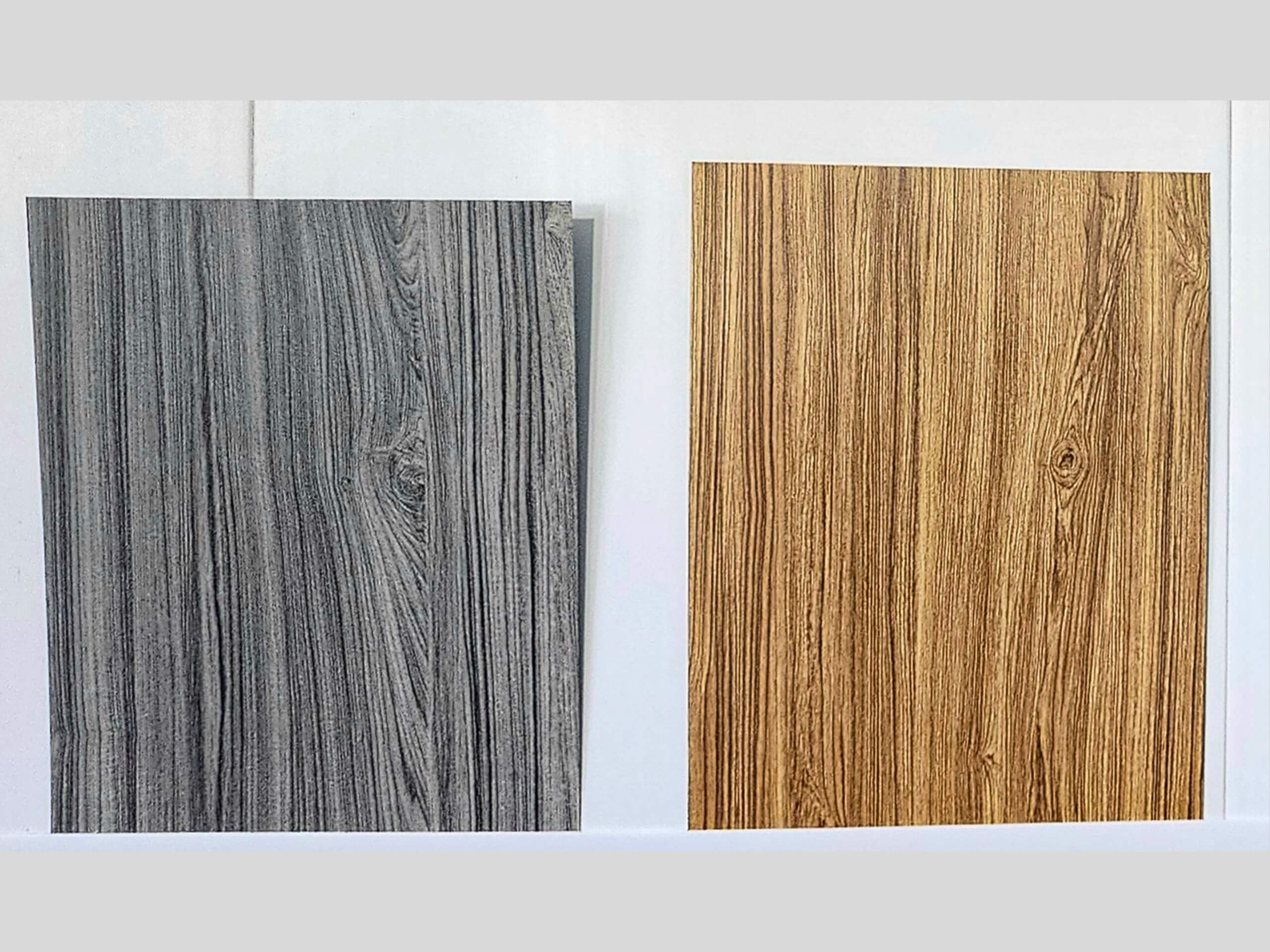 Sunset Metal Roofing and Siding Show Room Ebensburg, PA Two rectangular wood panels side by side; the left panel is gray with a wood grain pattern, and the right panel is light brown with a wood grain pattern. Both are set against a white background.