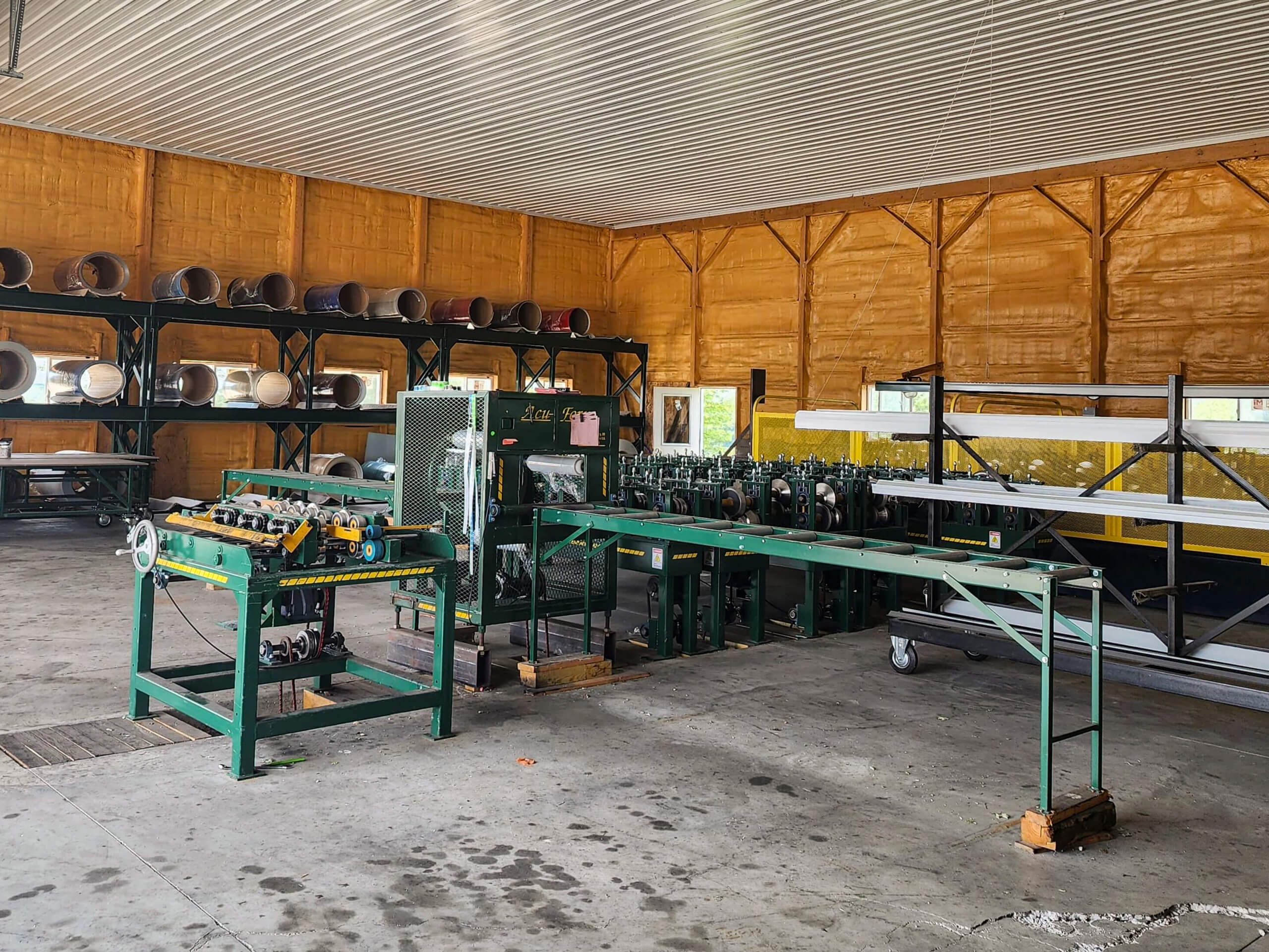 Sunset Metal Roofing and Siding Warehouse Ebensburg, PA Metalworking machinery and long metal sheets are arranged inside a spacious workshop with yellow walls and shelving units holding metal pipes.